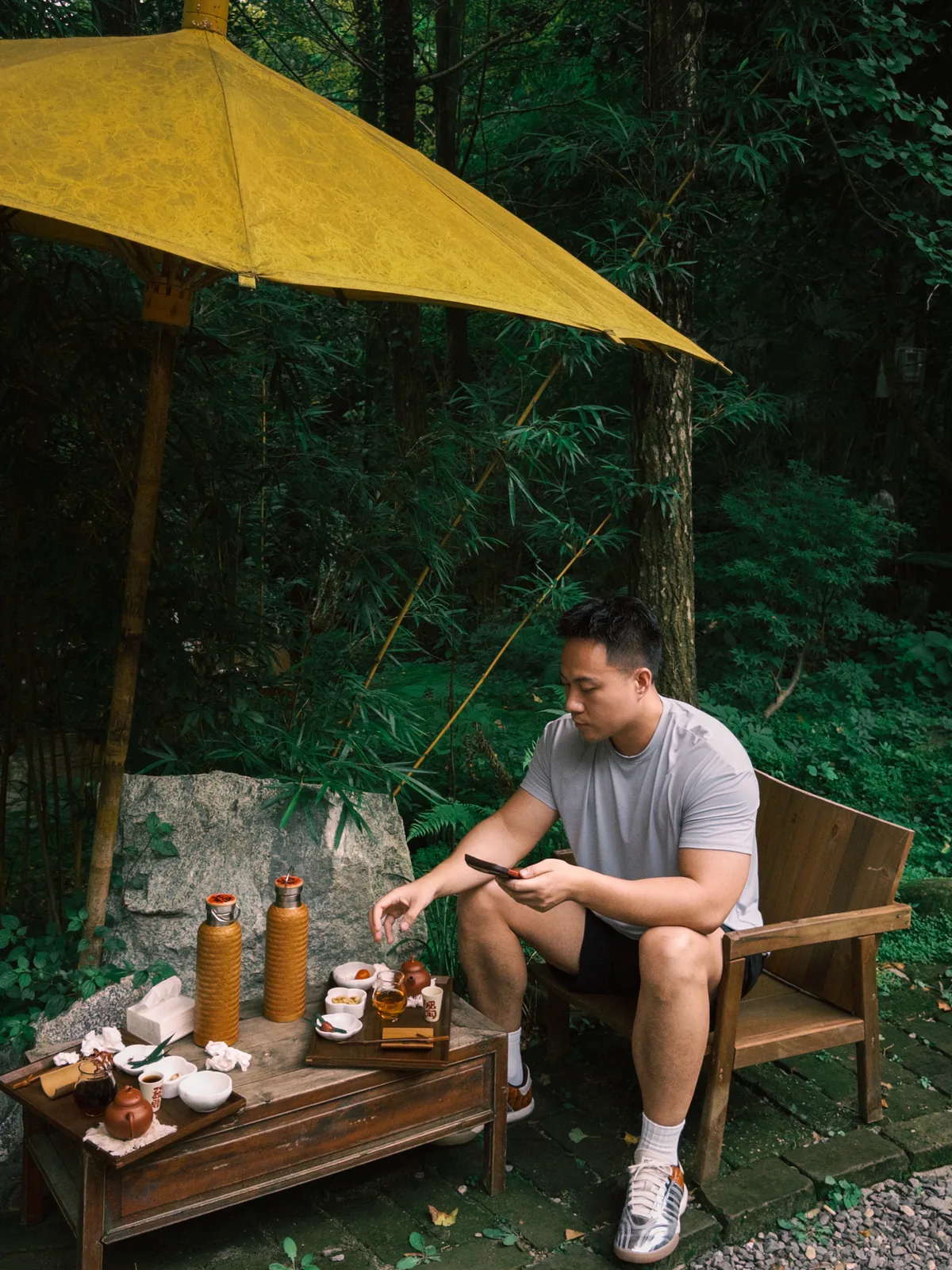 青城山男子坐户外长椅看手机，旁有茶具
